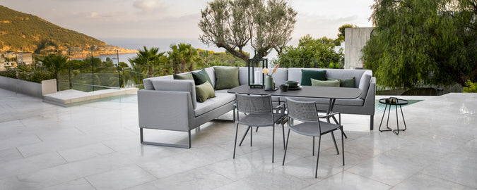 Espace lounge extérieur moderne avec canapé gris, coussins verts, table noire et chaises grises.