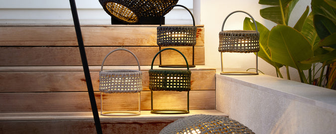 Une collection de lanternes noires, grises et vertes sur des marches en bois avec de la verdure.