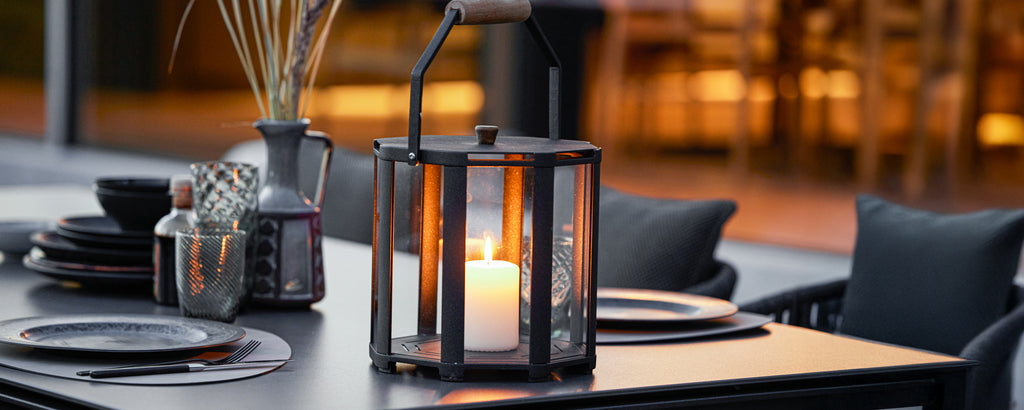 Lanterne noire avec bougie et vaisselle noire sur une table à manger moderne.