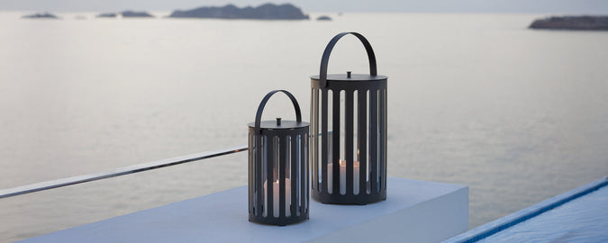 Deux lanternes noires modernes sur une surface surplombant un paysage maritime serein.