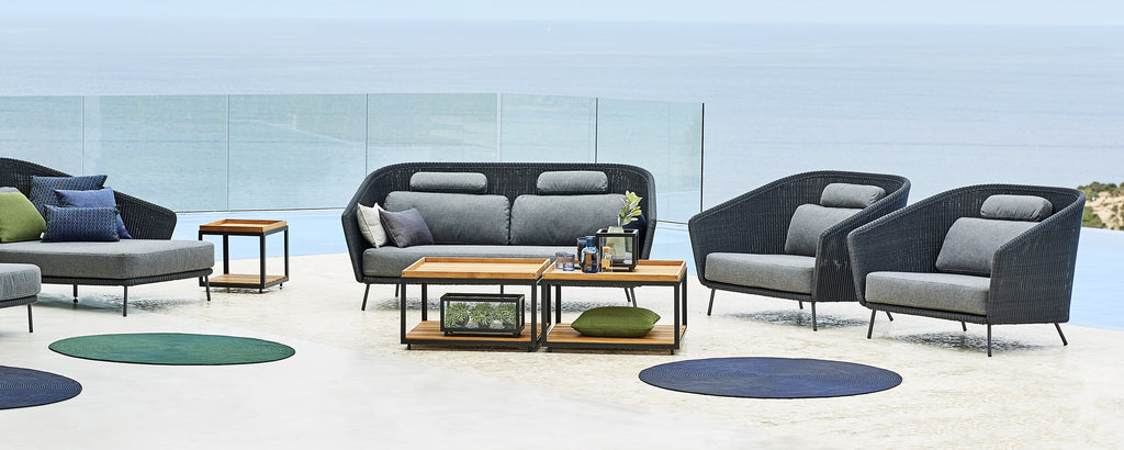 Espace salon moderne avec canapé gris, fauteuils noirs et table basse en bois.