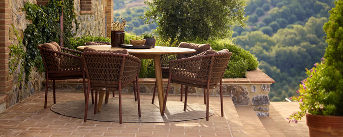 Chaises brunes entourant une table ronde sur une terrasse pittoresque avec de la verdure.