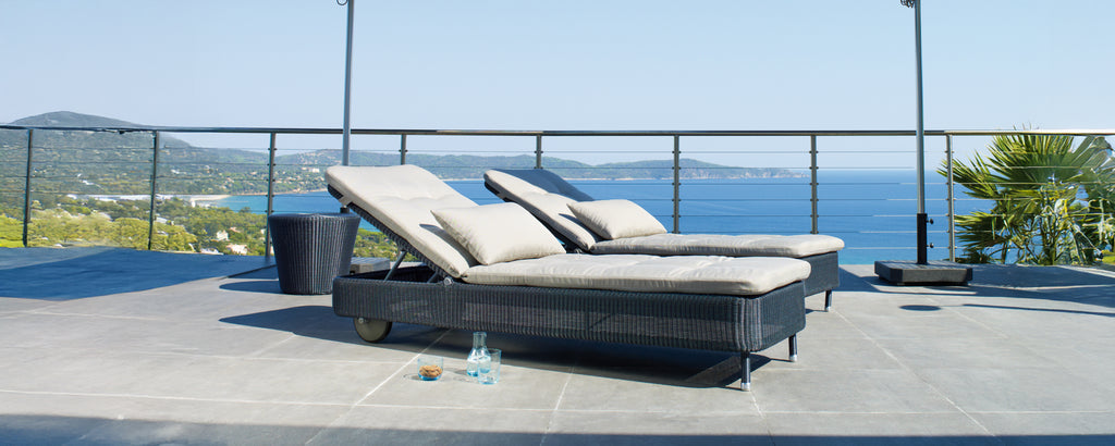 Deux chaises lounge modernes grises et noires sur une terrasse surplombant l'océan.
