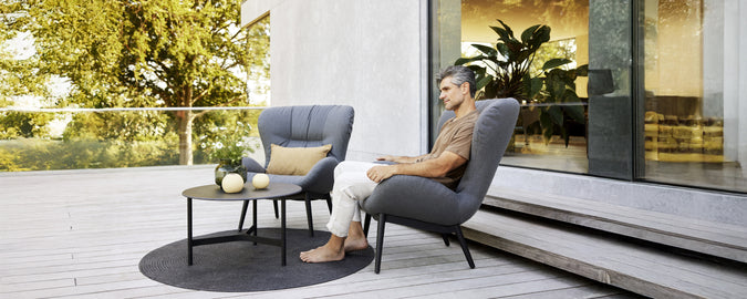 Espace lounge moderne avec des fauteuils gris, une table noire et un tapis rond.