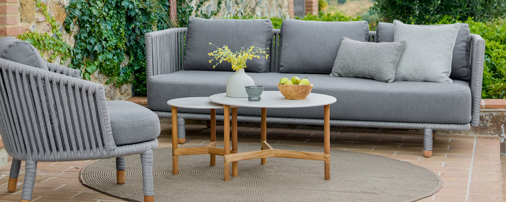 Espace lounge moderne en extérieur avec un canapé gris, une chaise grise et une table basse en bois.