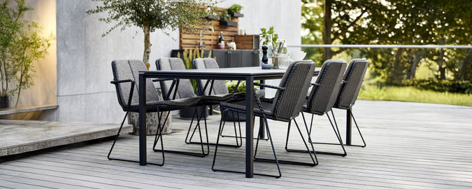 Table à manger noire avec des chaises grises dans un cadre extérieur moderne.
