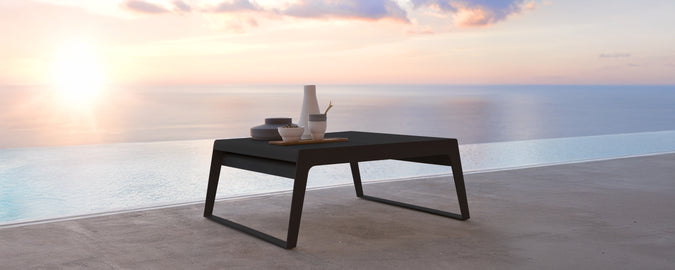 Table noire moderne sur une terrasse avec vue sur le coucher de soleil sur l'eau.