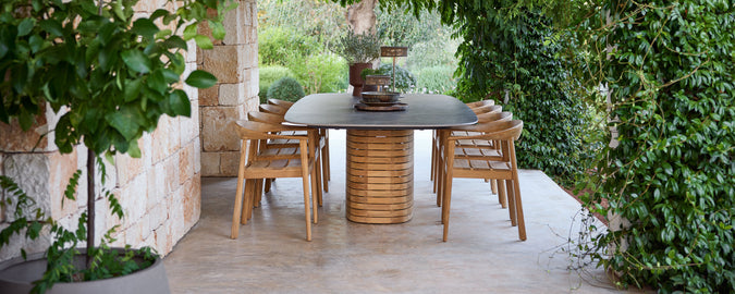 Des chaises en bois d'extérieur autour d'une table noire dans un jardin vert.