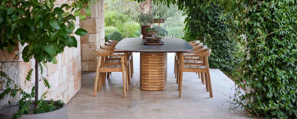 Des chaises en bois d'extérieur autour d'une table noire dans un jardin vert.