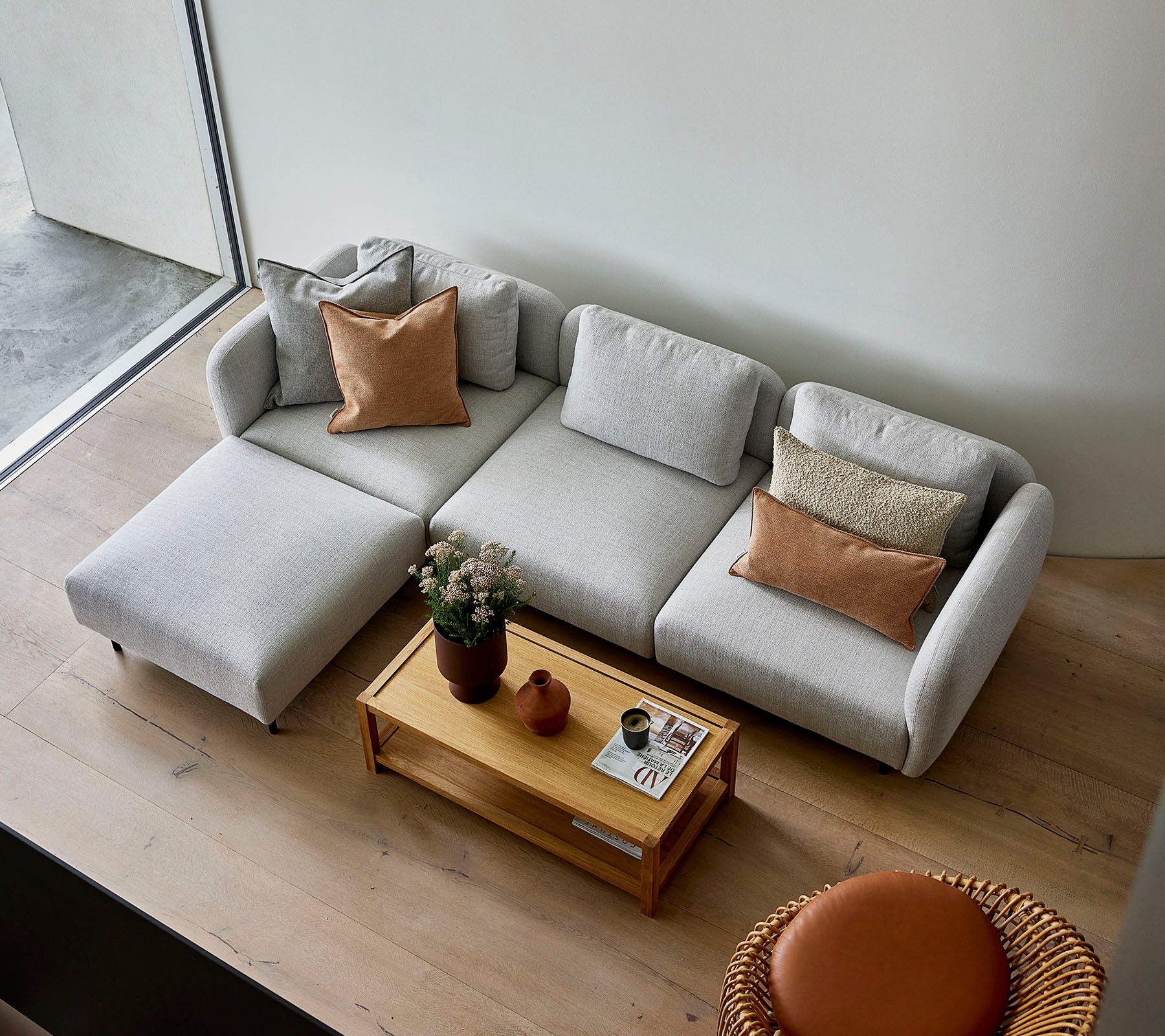 Un canapé d'angle gris clair au style élégant avec des coussins, associé à une table basse en bois et une option de siège ronde, créant une atmosphère accueillante.