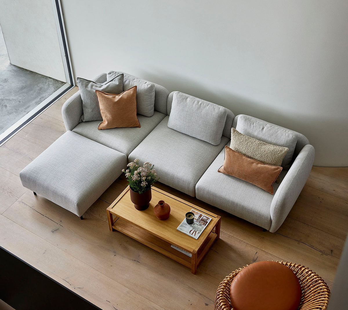 Un canapé d'angle gris clair au style élégant avec des coussins, associé à une table basse en bois et une option de siège ronde, créant une atmosphère accueillante.
