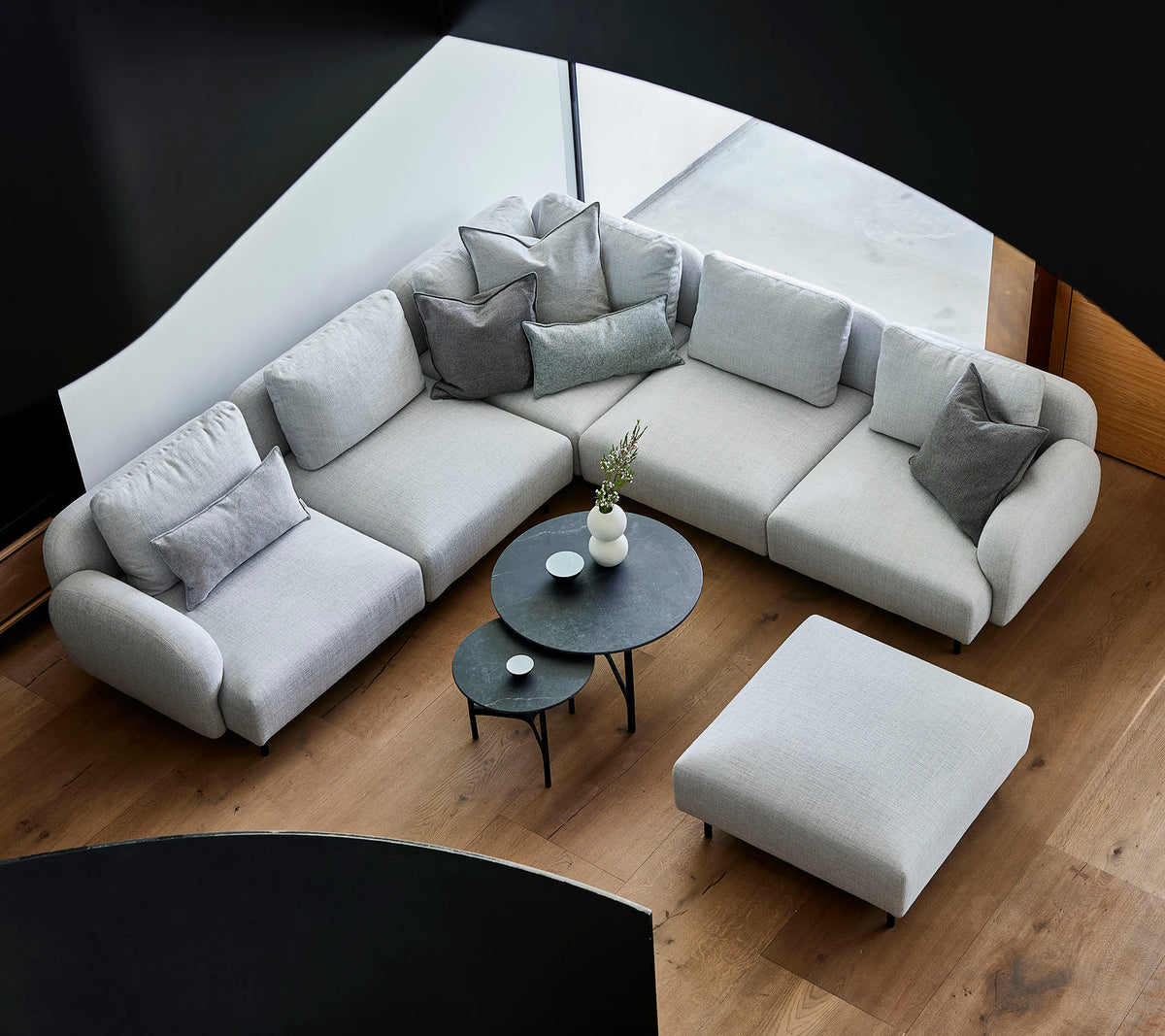 Canapé sectionnel gris élégant avec des coussins décoratifs, accompagné d'une table basse ronde chic et d'un pouf sur un sol en bois.