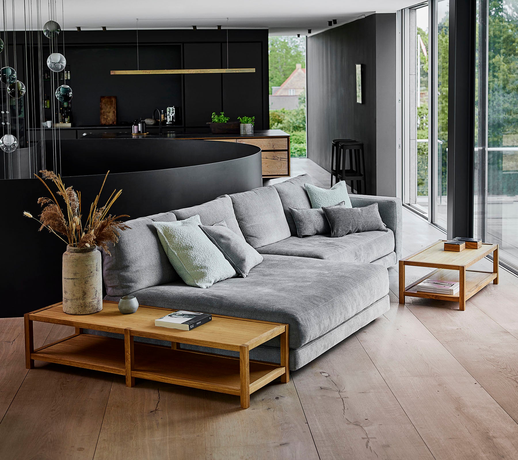 Espace de vie moderne avec un canapé d'angle gris orné de coussins, complété par des tables basses en bois et des arrangements de plantes décoratives.