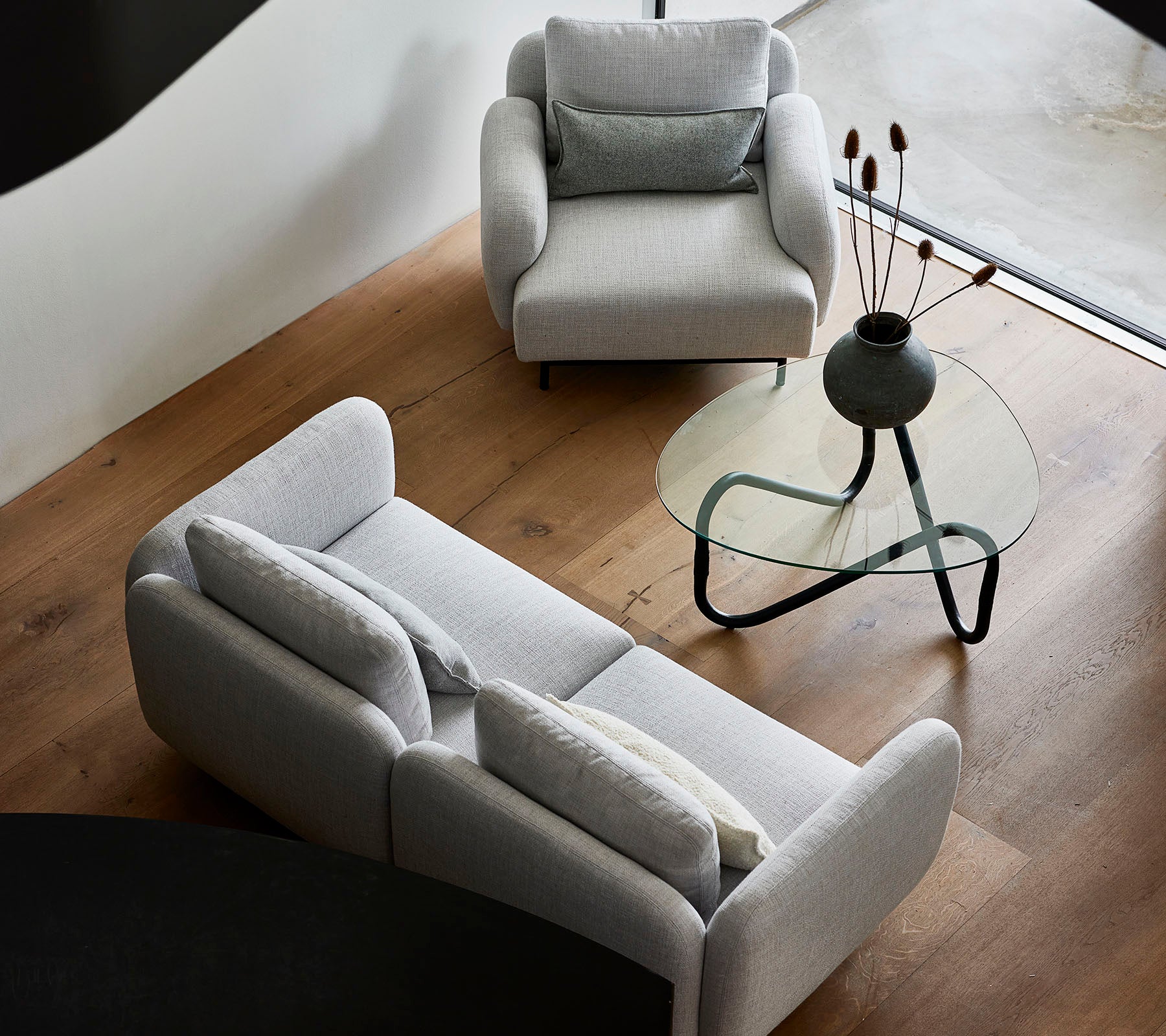 Canapés gris élégants et une table basse en verre élégante, avec des éléments décoratifs sur le plateau, contre un parquet en bois chaud.