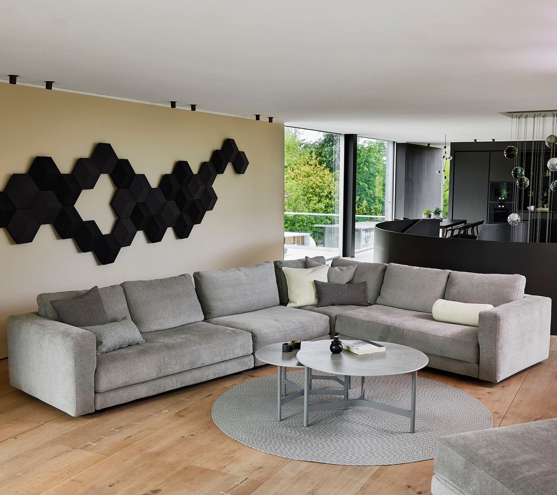 Un canapé sectionnel moderne gris avec des coussins décoratifs, une table basse ronde et une œuvre d'art mural texturée en noir.