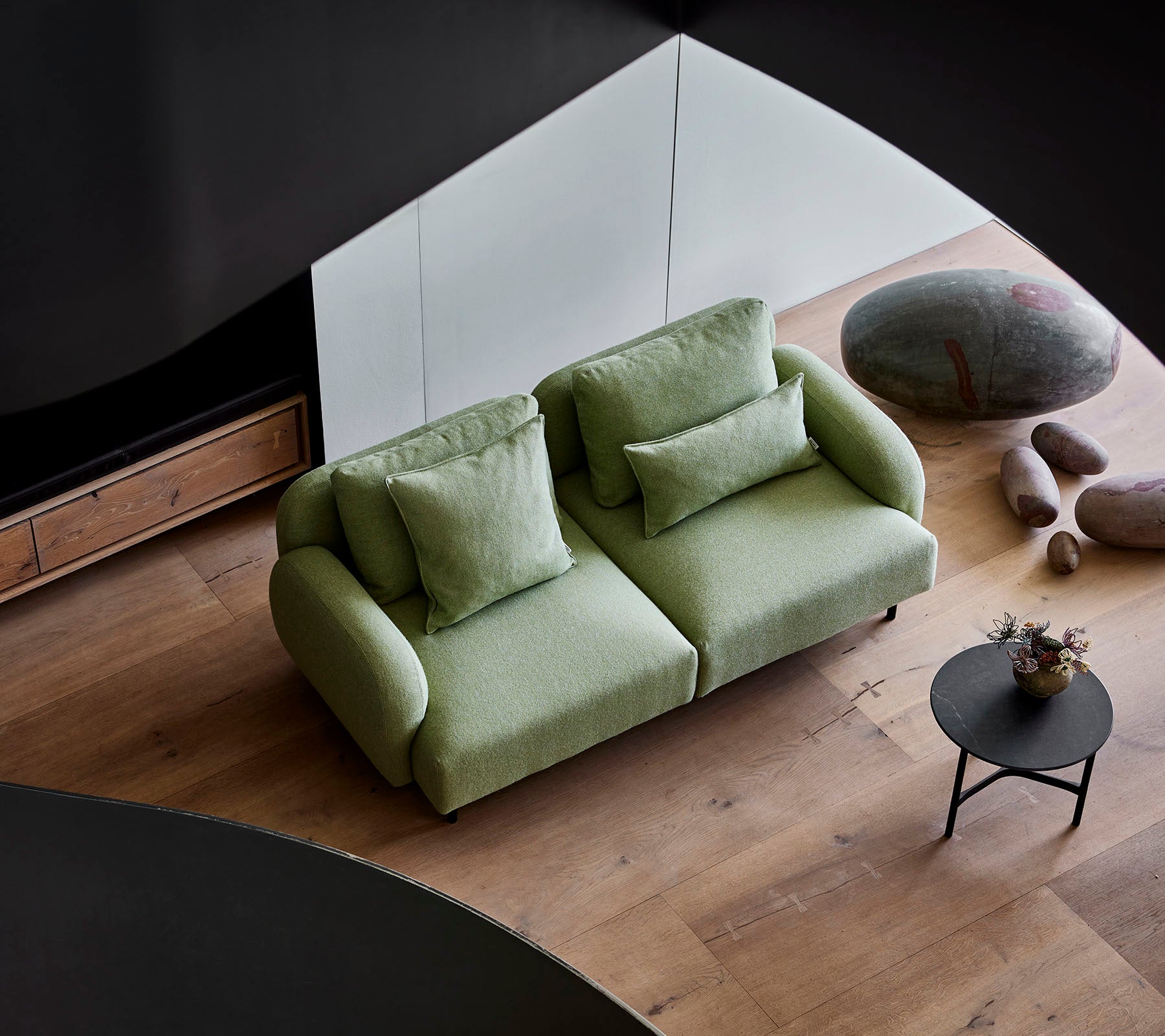 Canapé vert élégant avec des coussins moelleux à côté d'une petite table ronde, dans un cadre moderne avec un parquet en bois et des pierres lisses.