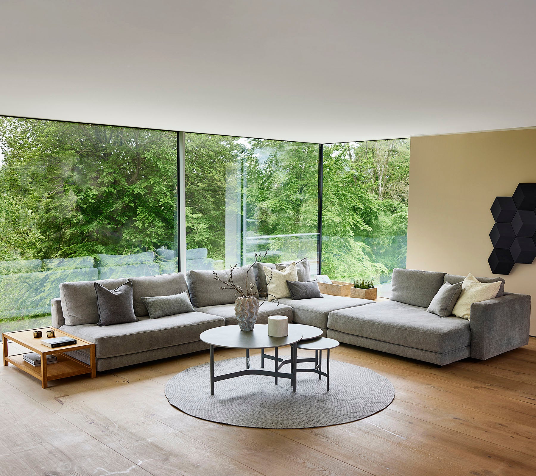 Un espace de vie moderne avec un canapé d'angle gris, une table basse ronde et de grandes fenêtres qui mettent en valeur la lumière naturelle.