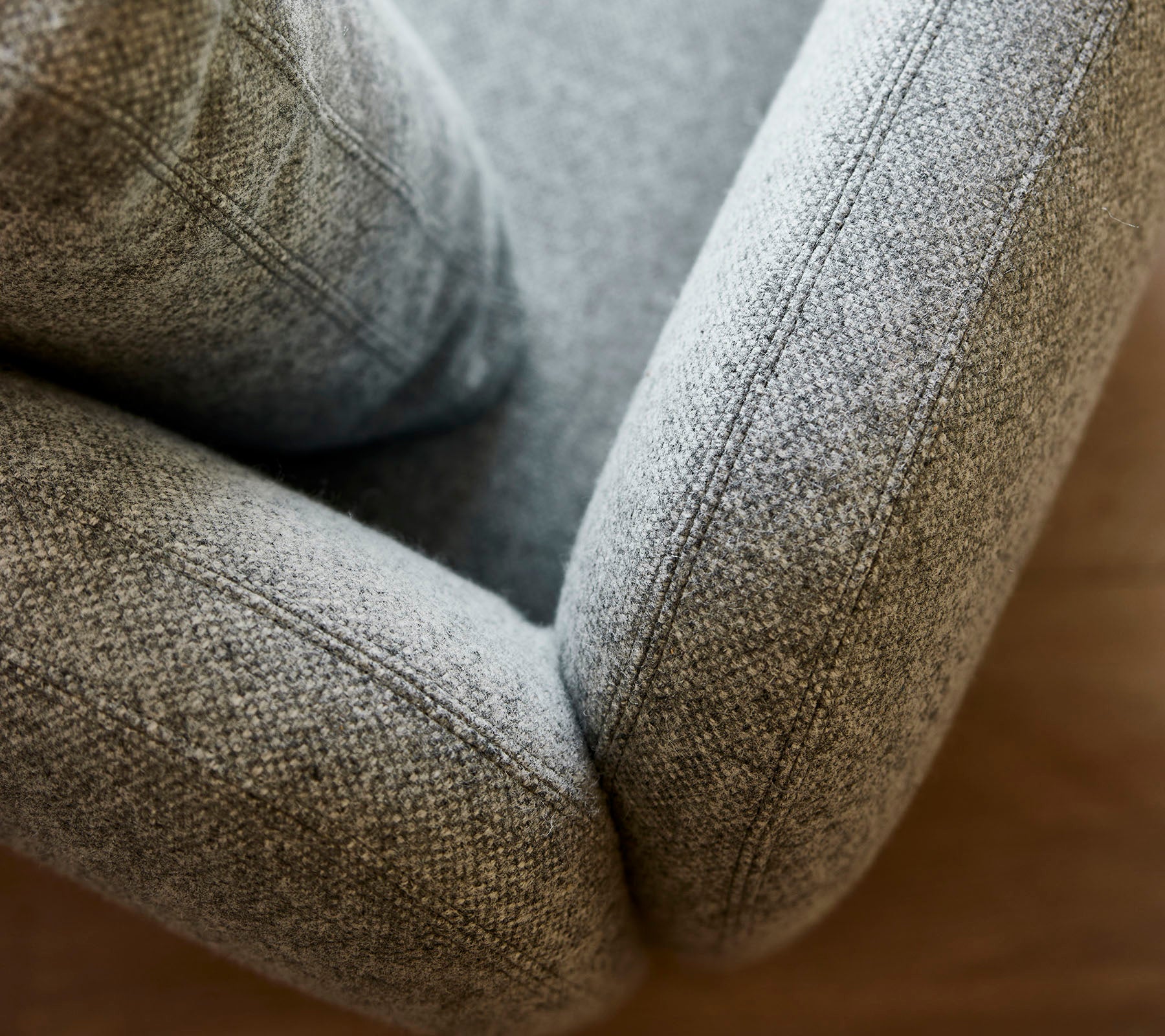 Gros plan d'un fauteuil en tissu gris doux et texturé, mettant en valeur ses courbes lisses et ses coutures détaillées.