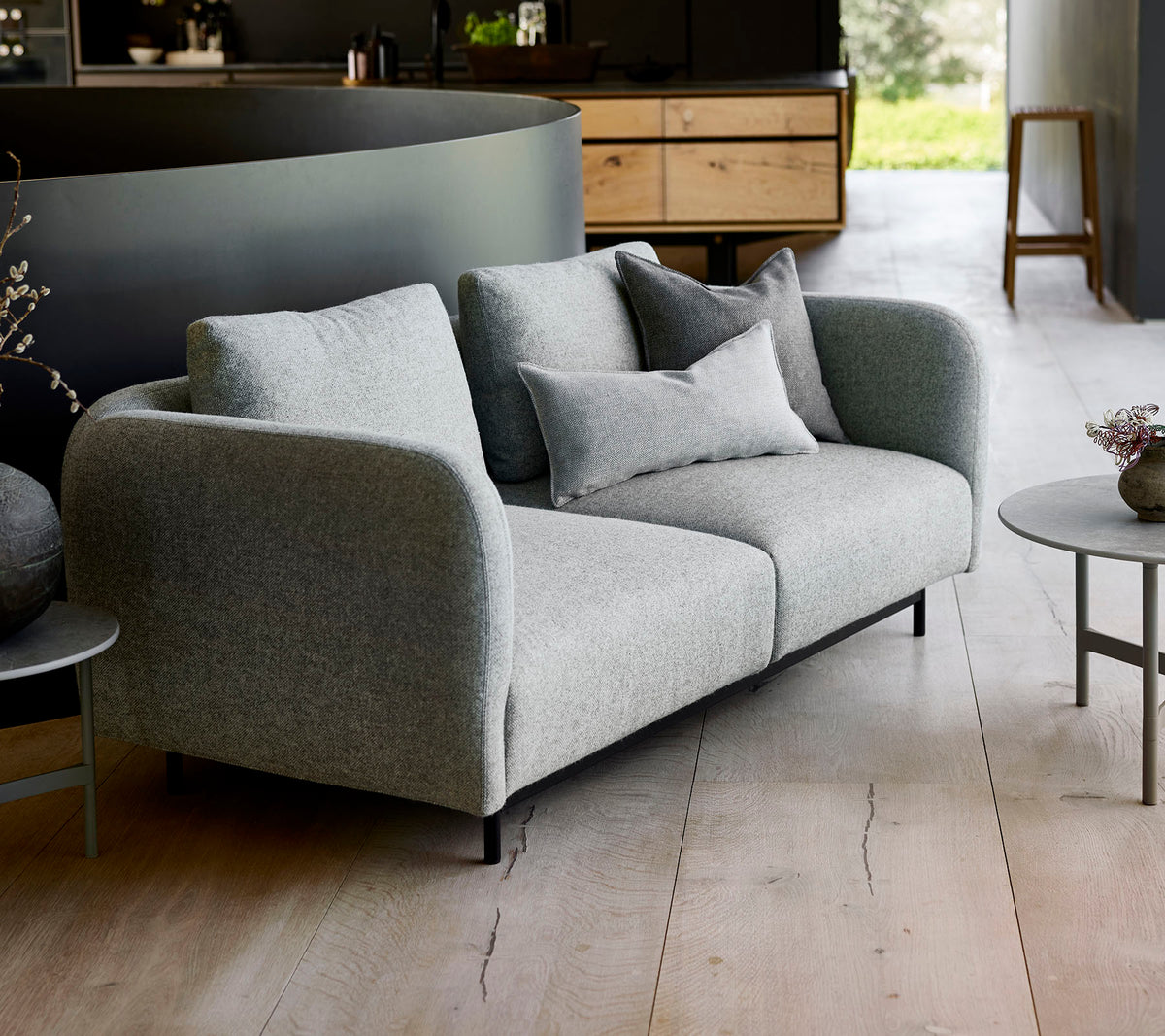 Canapé gris moderne avec des coussins moelleux, associé à une petite table ronde, sur un fond minimaliste.