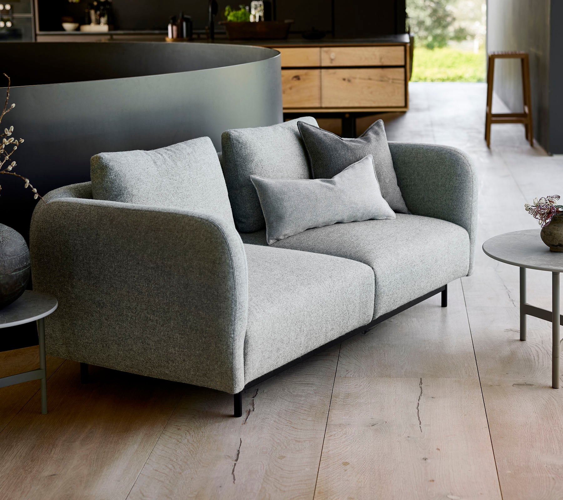 Canapé gris moderne avec des coussins moelleux, associé à une petite table ronde, sur un fond minimaliste.