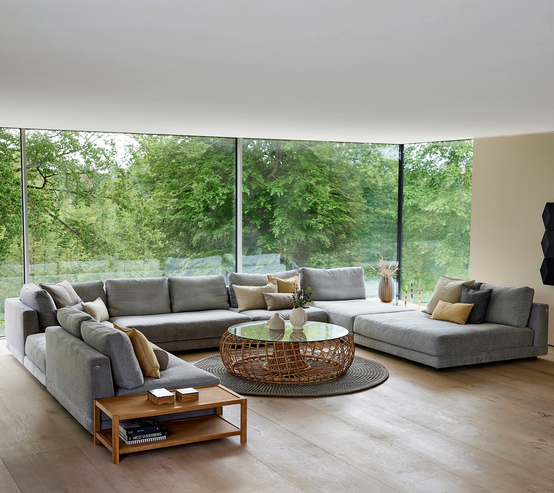 Espace de vie spacieux avec un grand canapé d'angle, une table basse et des accents décoratifs, entouré de lumière naturelle et de verdure.