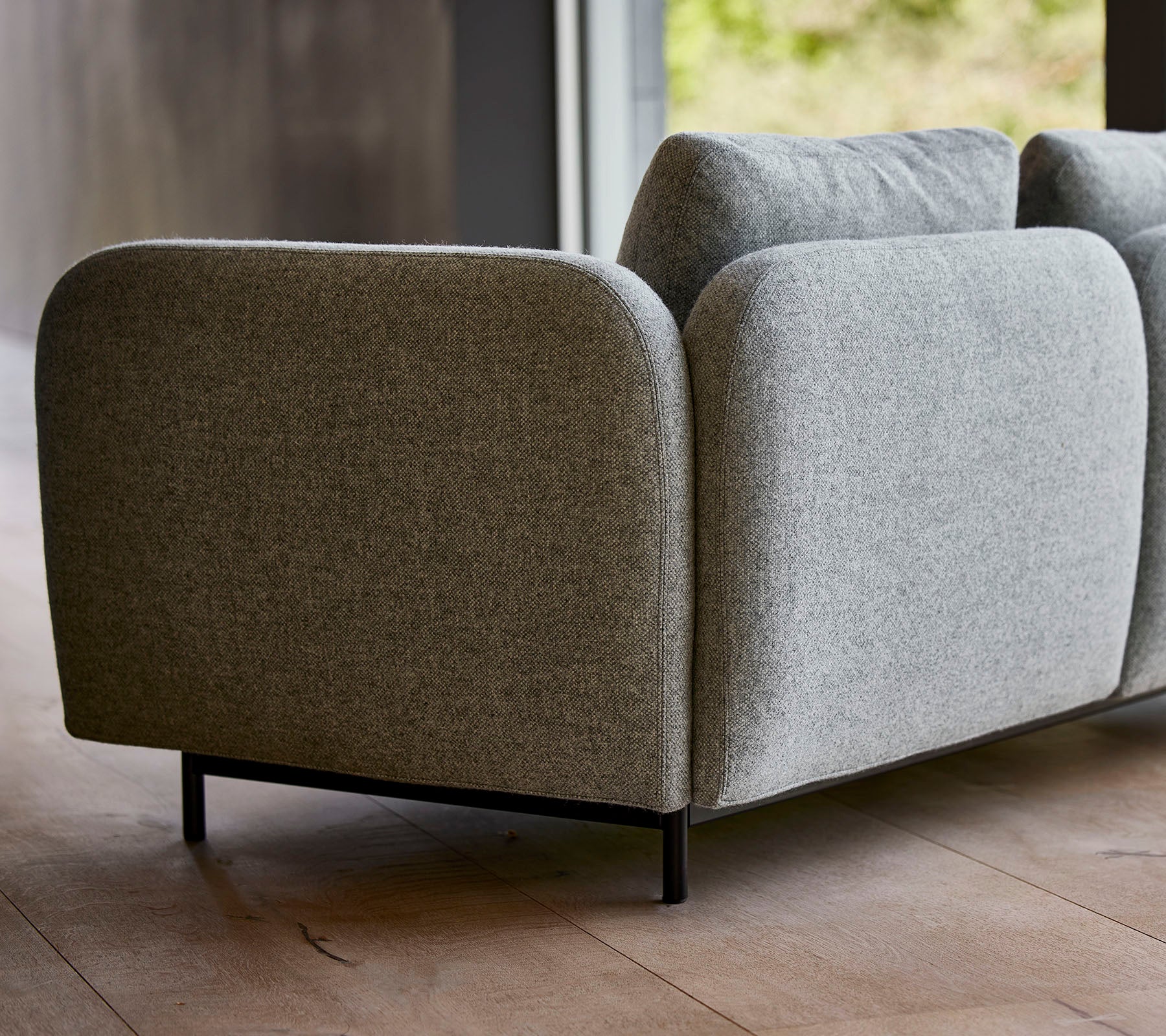 Un canapé moderne en tissu gris avec des bords arrondis et des pieds noirs élégants, présentant un design minimaliste.