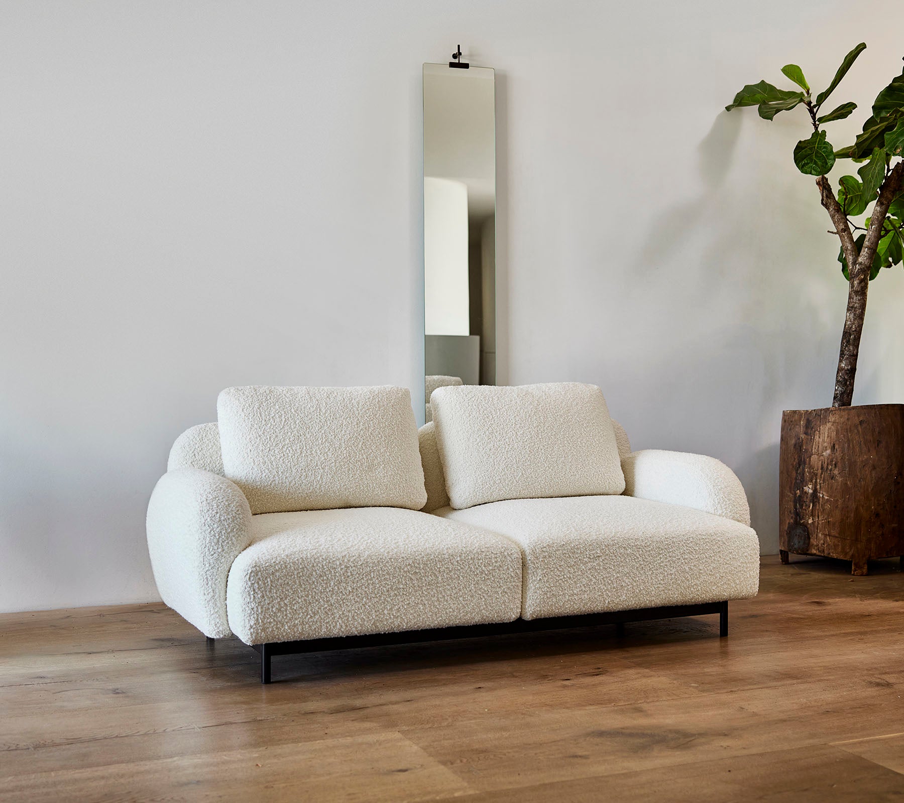 Un canapé blanc élégant avec des coussins moelleux, associé à un grand miroir et à une plante en pot dans un cadre moderne.