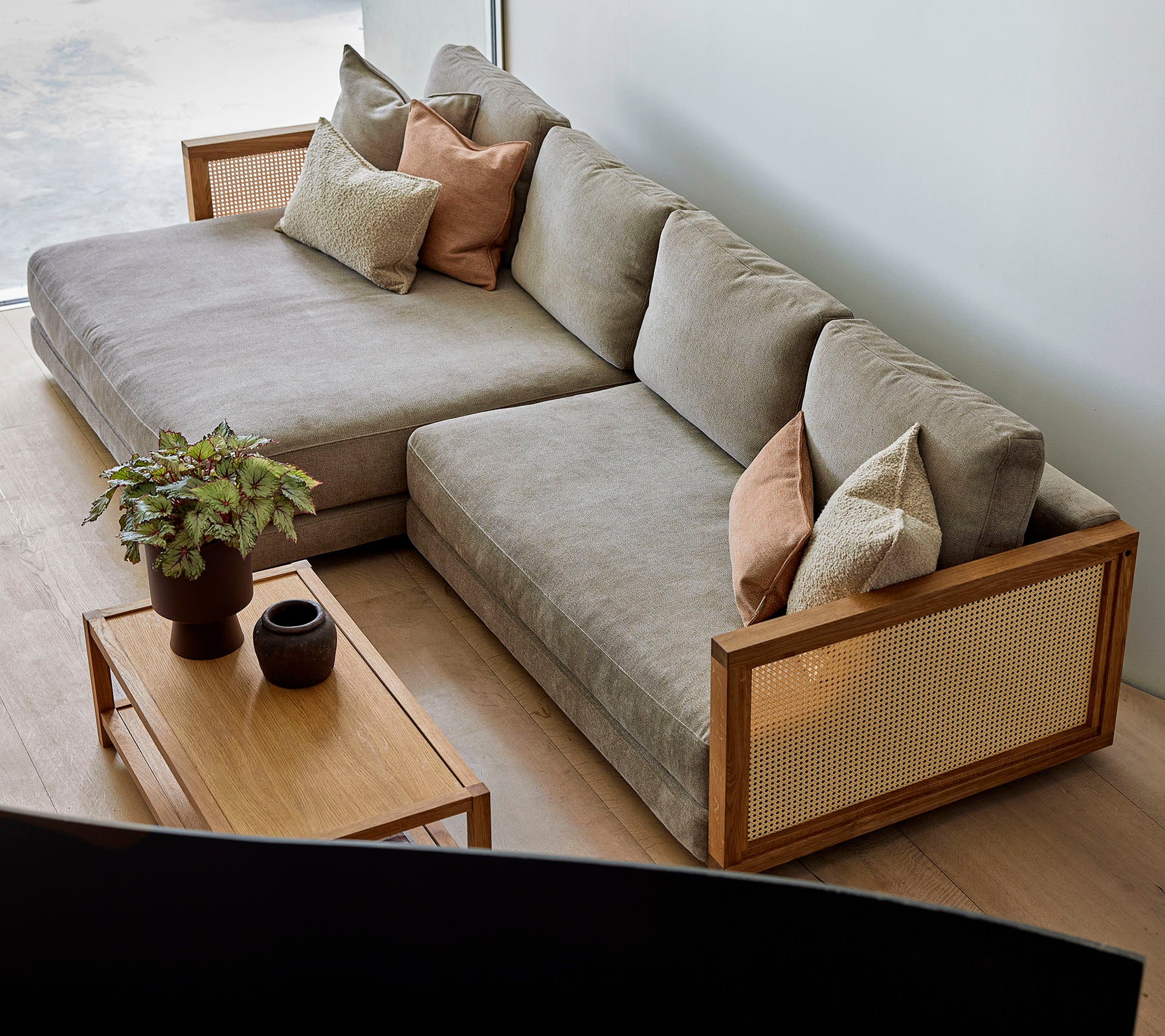 Un canapé sectionnel élégant avec des coussins doux et des coussins décoratifs, associé à une table basse en bois ornée de plantes et de décorations élégantes.