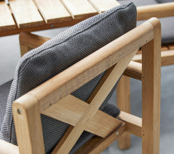 Chaise en bois avec un coussin à motif gris, présentant un design croisillon sur le dossier et entourée de lattes en bois.