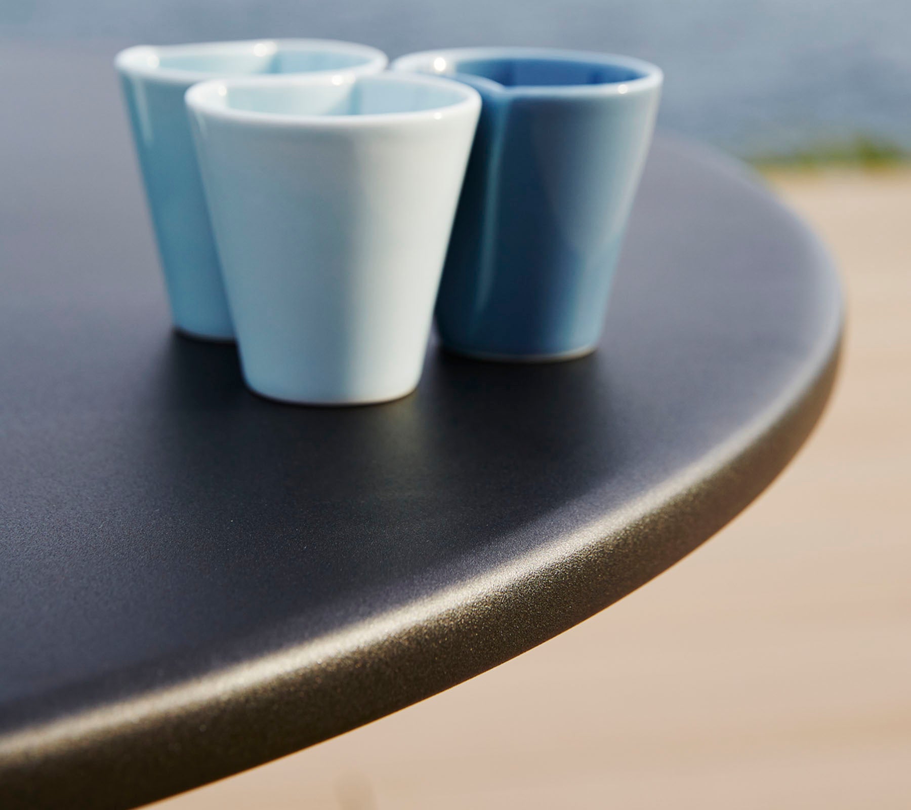 Trois petites tasses en céramique de différentes nuances de bleu reposent sur une surface de table ronde et lisse.