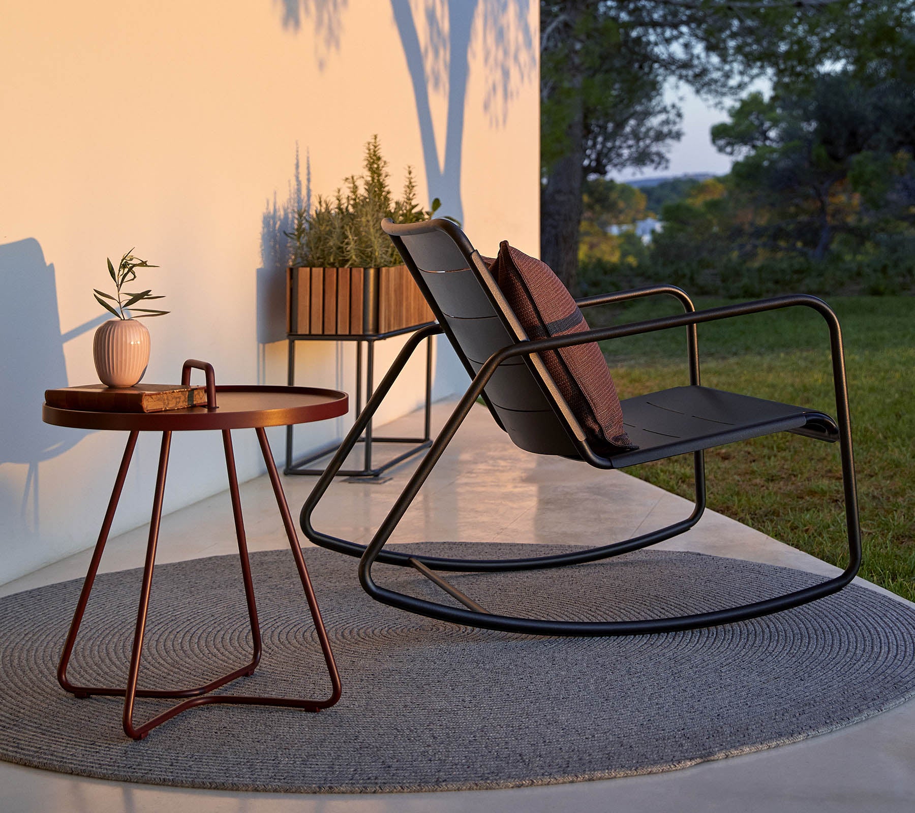 Un fauteuil à bascule élégant avec des coussins, accompagné d'une petite table ronde et d'une plante en pot, sur un fond serein.
