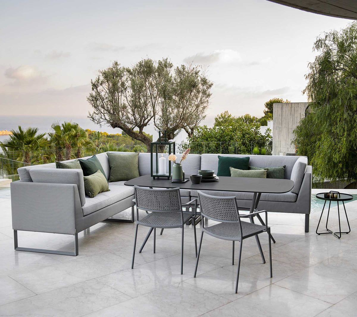 Espace extérieur moderne avec un canapé d'angle élégant, une table à manger et des chaises en métal entourées de verdure.