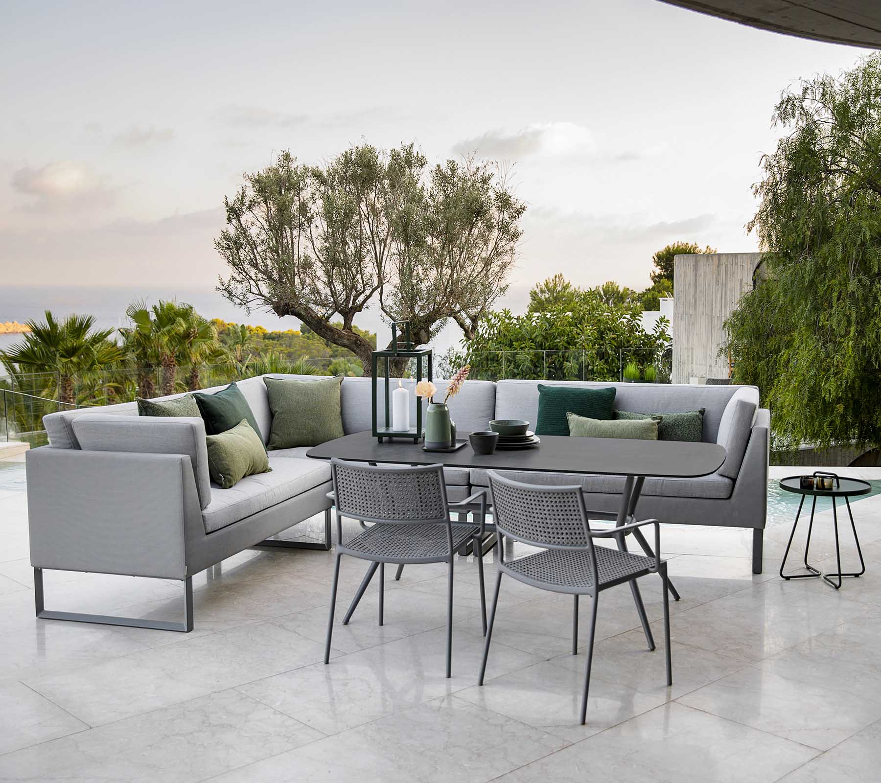 Espace extérieur moderne avec un canapé d'angle élégant, une table à manger et des chaises en métal entourées de verdure.