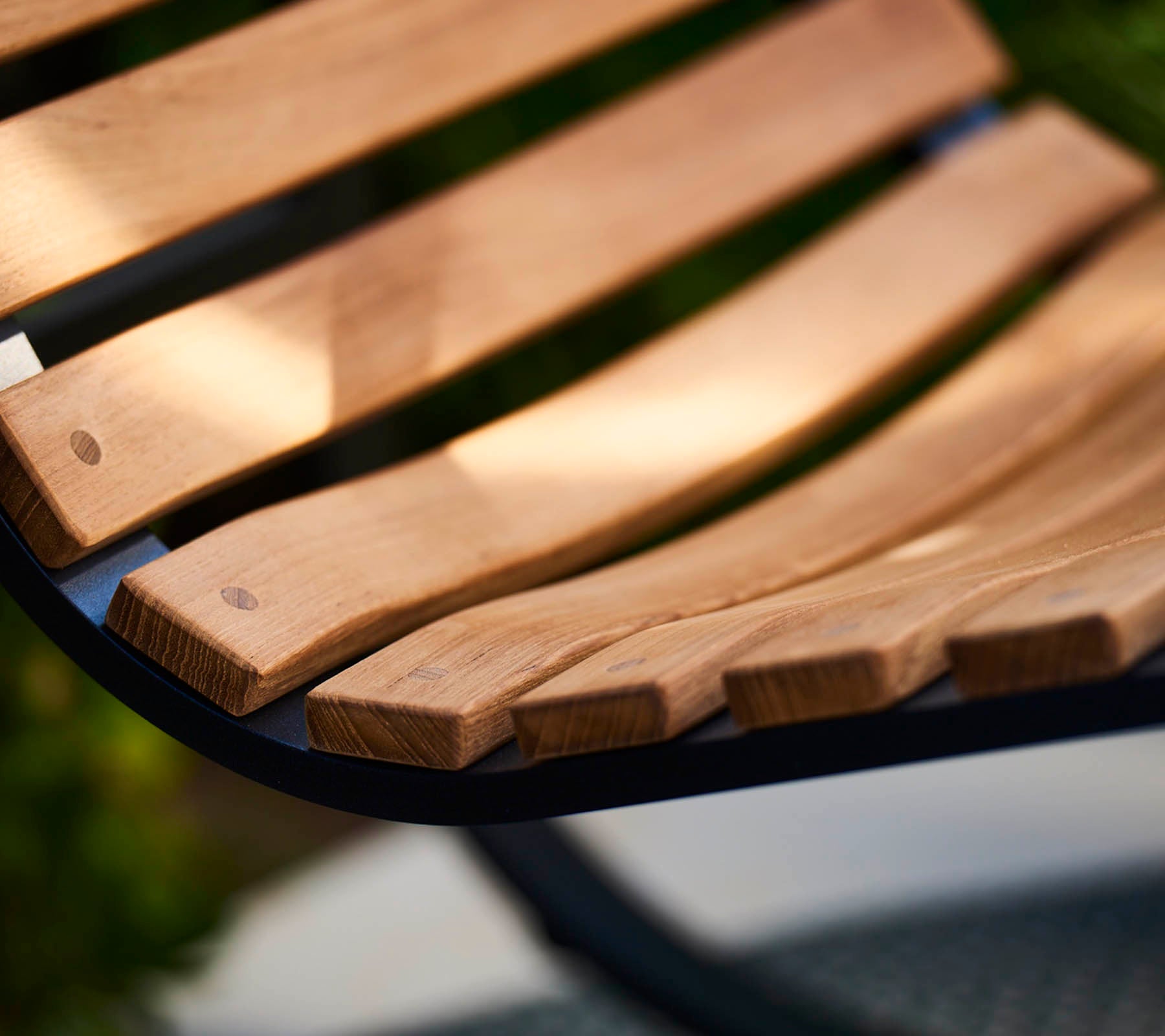 Gros plan d'une lame de banc en bois incurvée avec un grain de bois lisse et naturel, mettant en valeur l'artisanat et un design chaleureux et accueillant.
