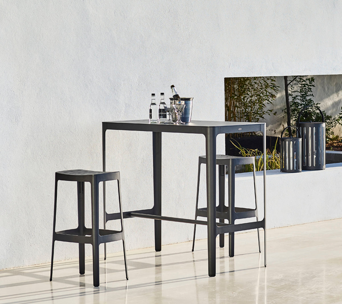 Une table élégante avec deux tabourets assortis, arborant un design minimaliste et des bouteilles placées dessus, sur un fond neutre.