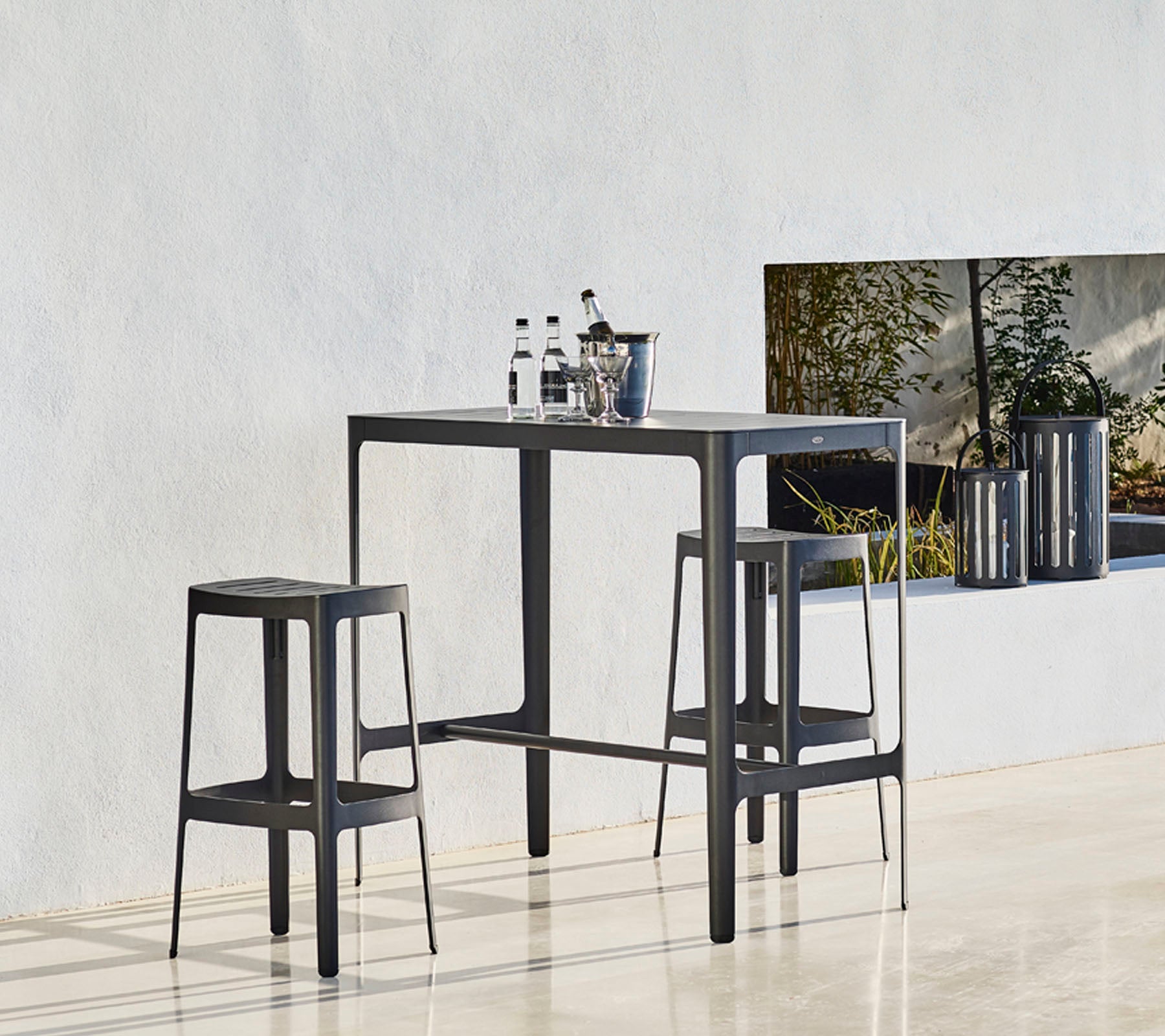 Une table élégante avec deux tabourets assortis, arborant un design minimaliste et des bouteilles placées dessus, sur un fond neutre.
