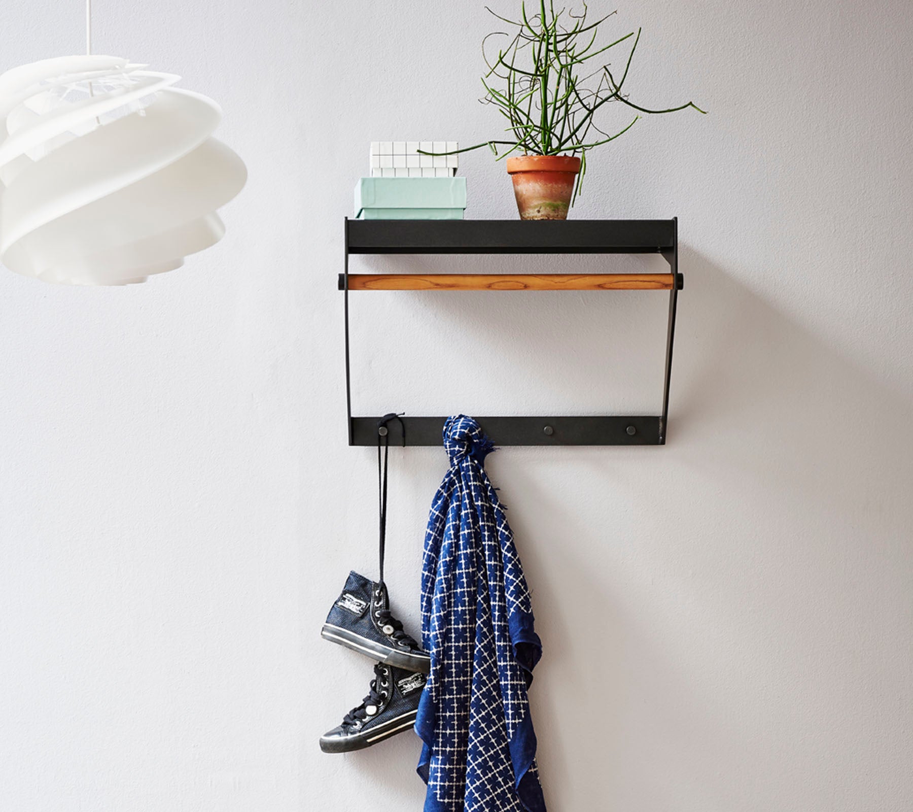 Étagère murale avec un dessus en bois, présentant une petite plante, une écharpe suspendue en dessous et une paire de chaussures au sol.