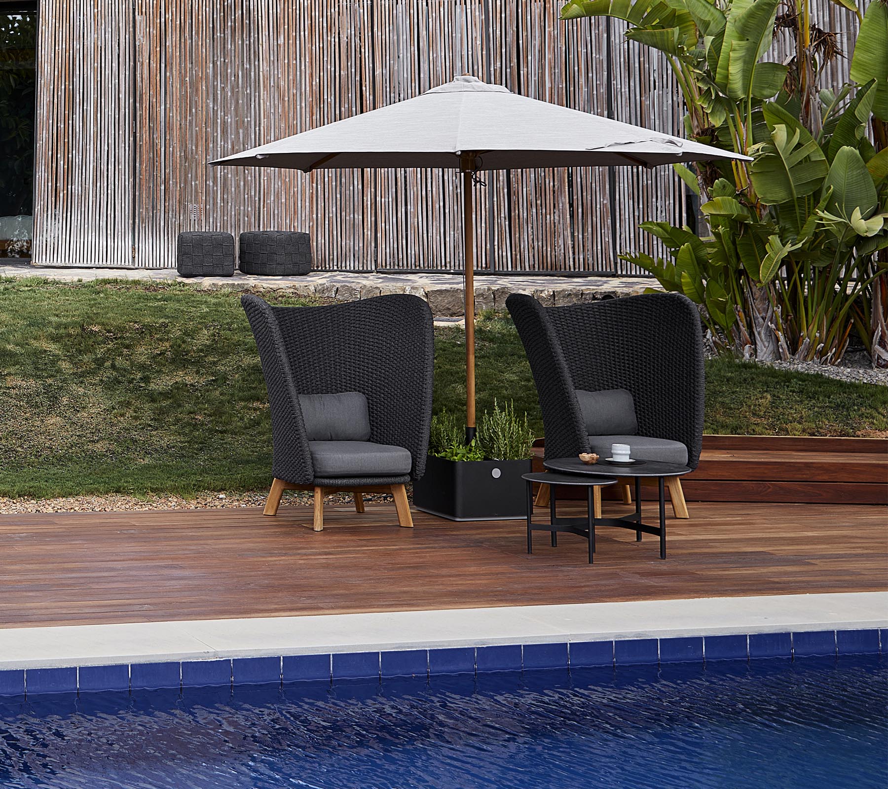 Deux chaises de jardin élégantes avec des coussins sous un grand parasol, accompagnées d'une petite table, à côté d'une piscine.