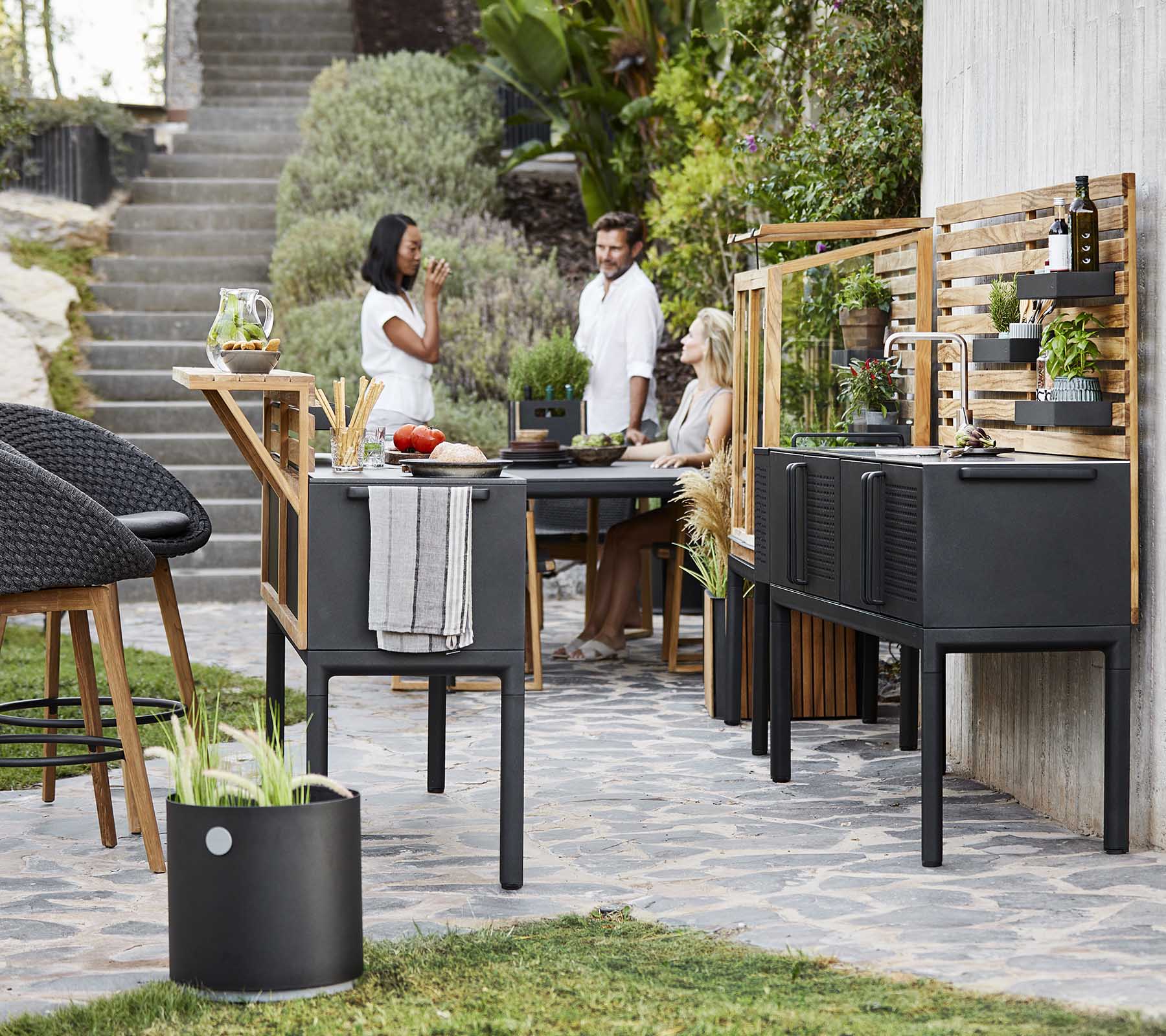 Un espace de restauration extérieur moderne avec des meubles noirs élégants, de la verdure et des gens appréciant un repas ensemble.