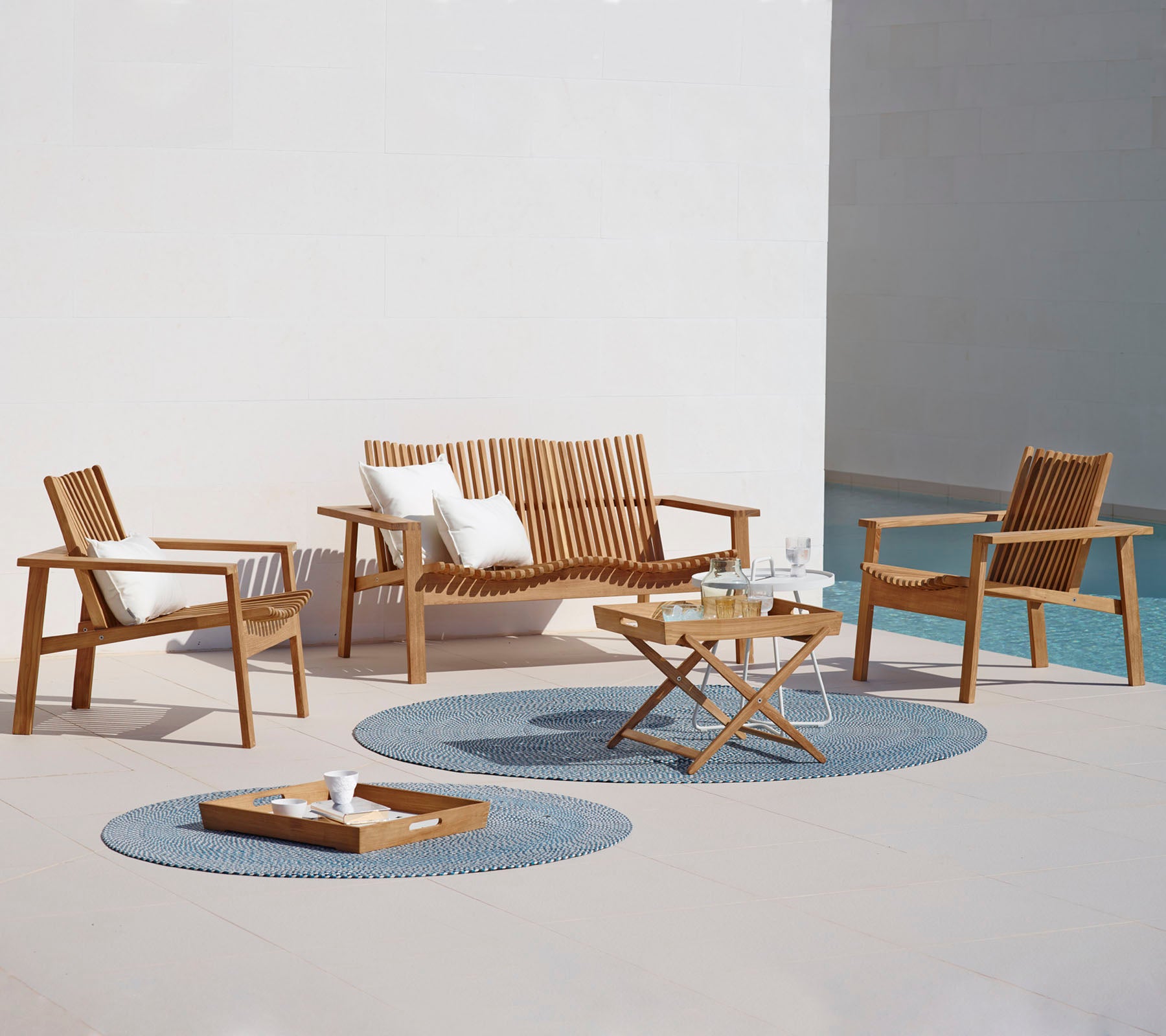 Un aménagement extérieur élégant avec un canapé, deux fauteuils, une table basse et des tapis décoratifs. Idéal pour se détendre.