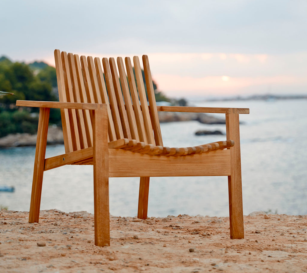 Une chaise en bois avec un dossier et un siège en lattes, positionnée près de l'eau, illustrant un cadre naturel et serein.