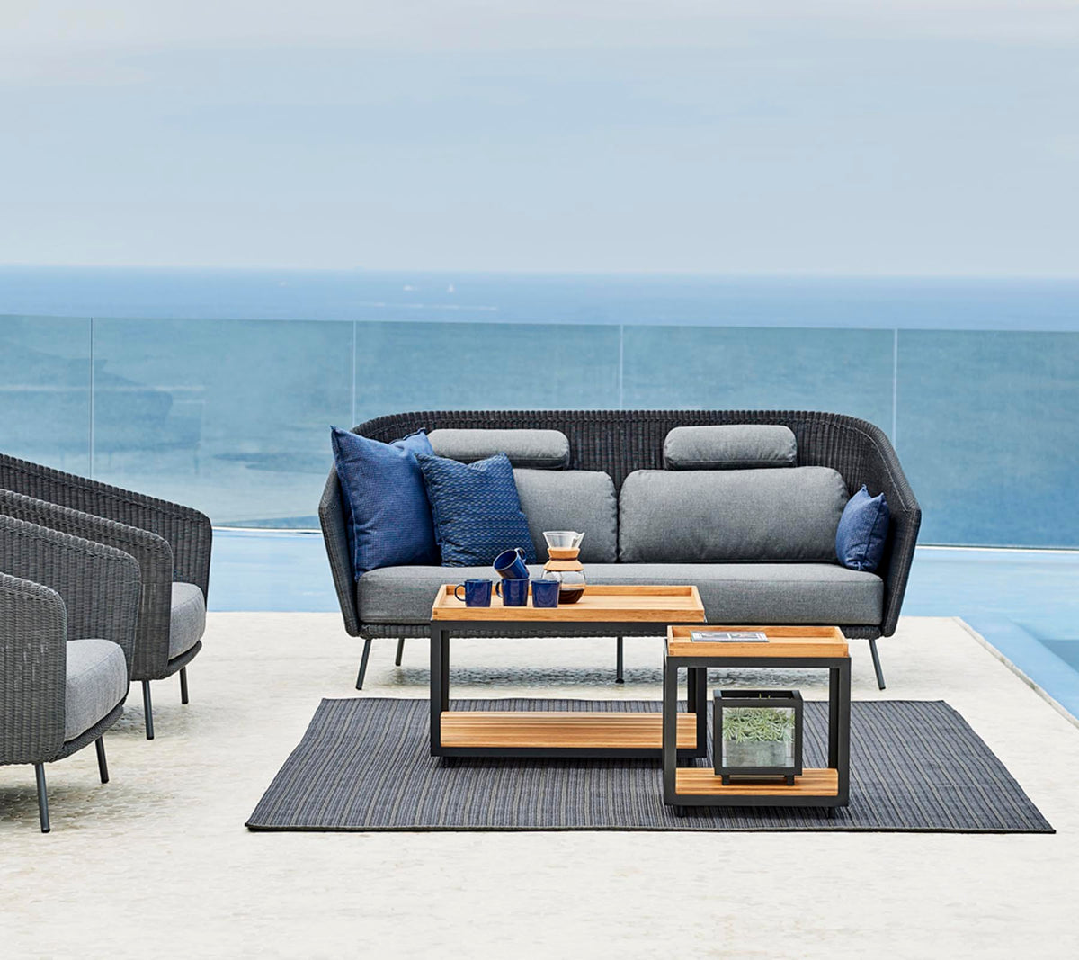 Agencement de sièges extérieur élégant avec un canapé gris et des coussins bleus, une table d'appoint en bois et un tapis assorti.