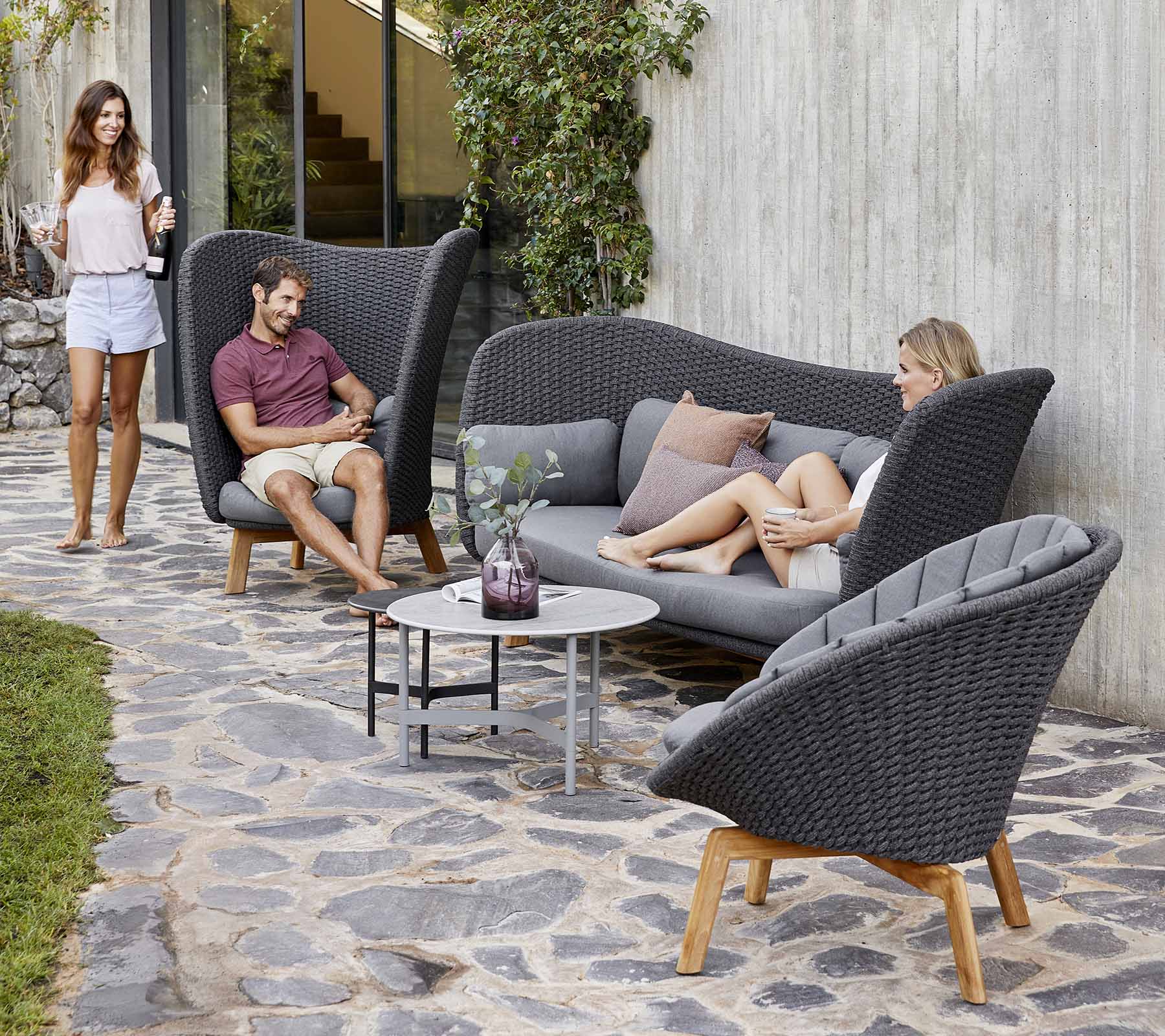 Agencement de sièges extérieurs élégant avec un canapé incurvé et des chaises, avec une petite table, entouré de verdure.