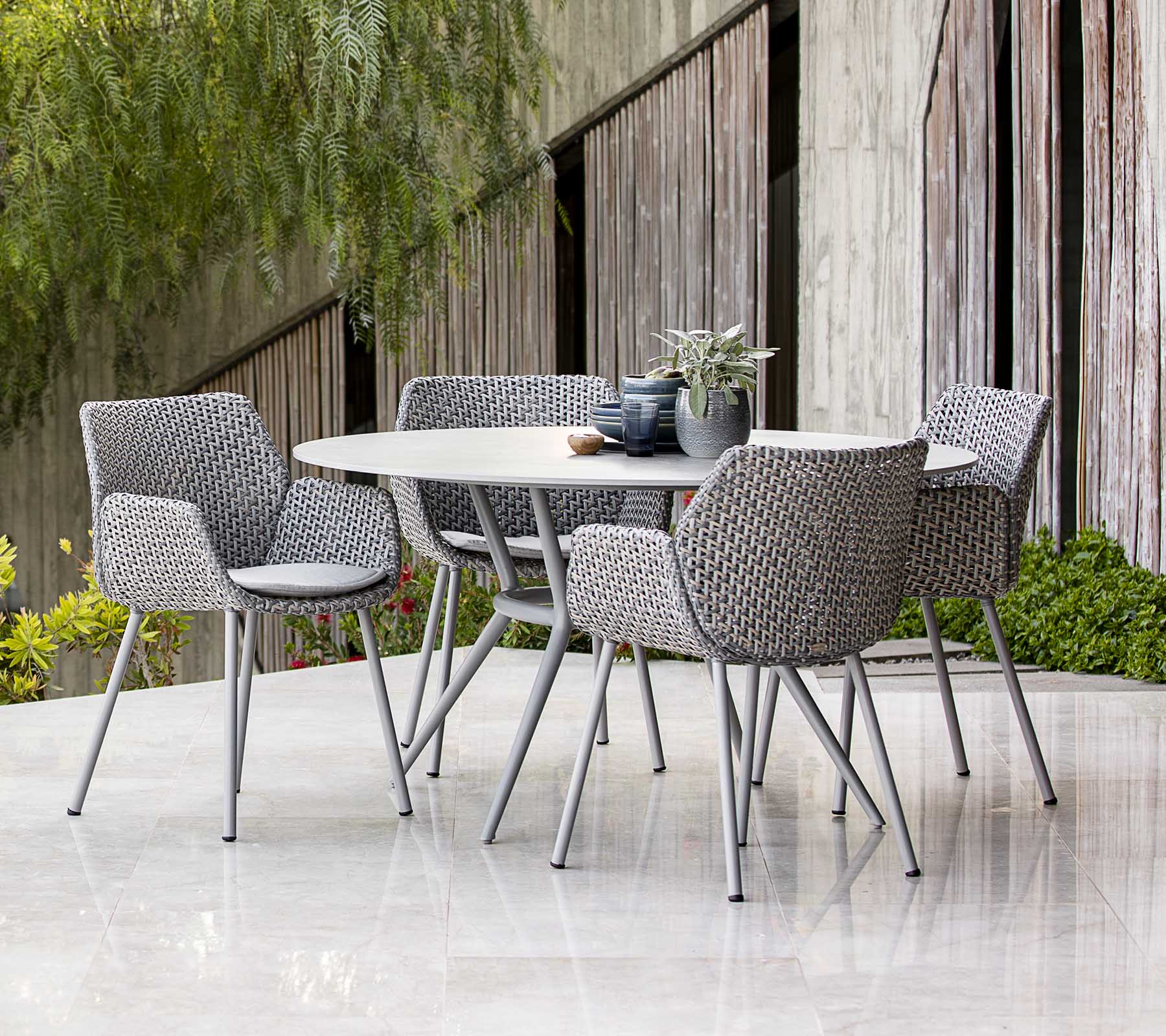 Ensemble de salle à manger d'extérieur contemporain avec des chaises tressées, agencé avec des plantes et une décoration de table, présentant une esthétique moderne.