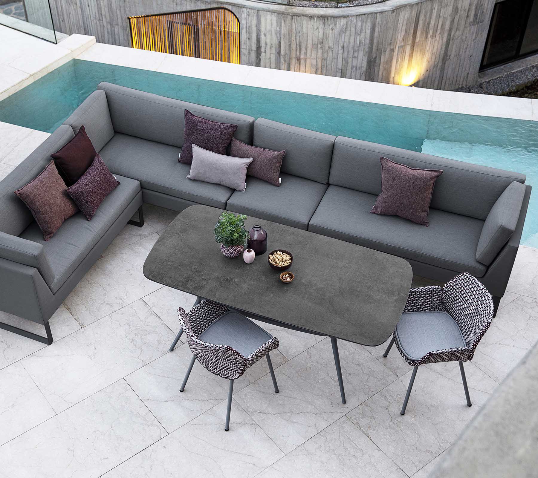 Agencement moderne de sièges extérieurs avec un canapé en section gris, des coussins décoratifs et une table à manger élégante entourée de chaises stylées.