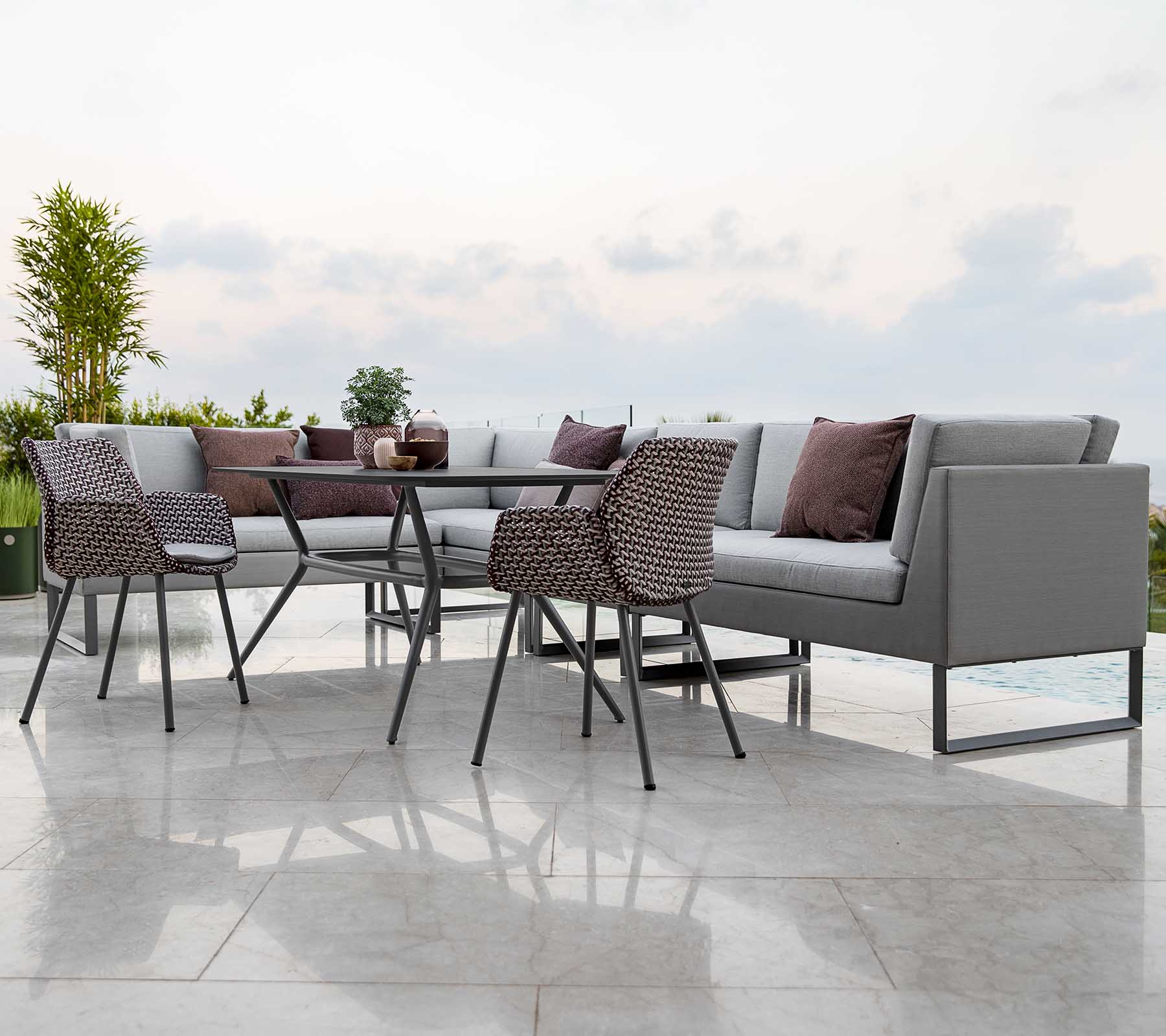 Agencement moderne de sièges d'extérieur comprenant un canapé sectionnel avec des coussins, une table en verre et des chaises élégantes.