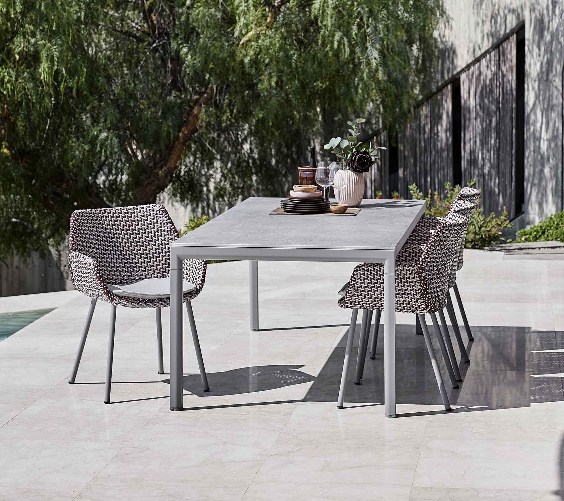 Une table à manger moderne entourée de chaises tressées élégantes, complétée par des vases décoratifs et de la verdure en arrière-plan.