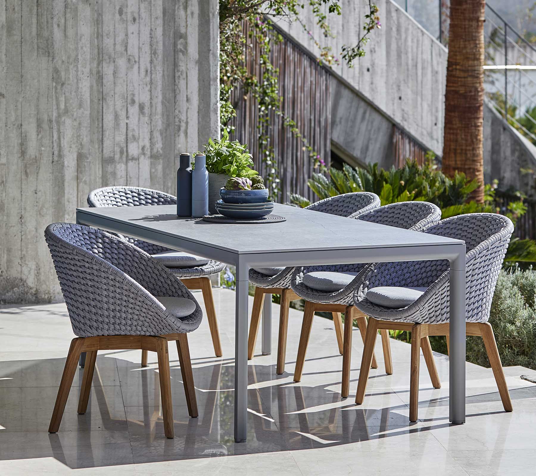 Ensemble moderne de salle à manger avec une table grise et des chaises tressées avec des pieds en bois, soigneusement disposé avec des objets décoratifs sur la table.