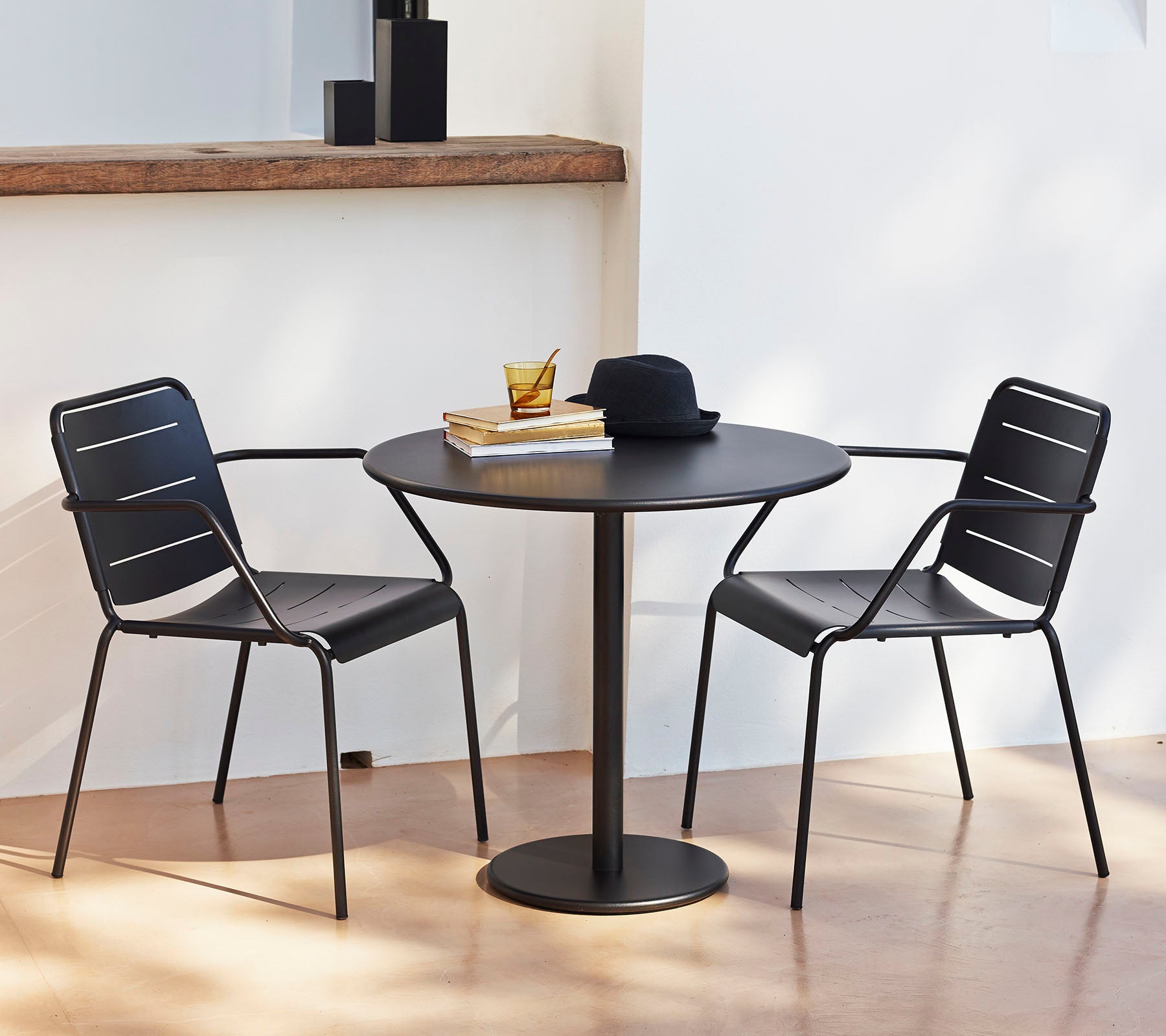 Une table ronde avec deux chaises noires, surmontée d'un chapeau et de livres, créant ainsi un coin salon élégant et accueillant.