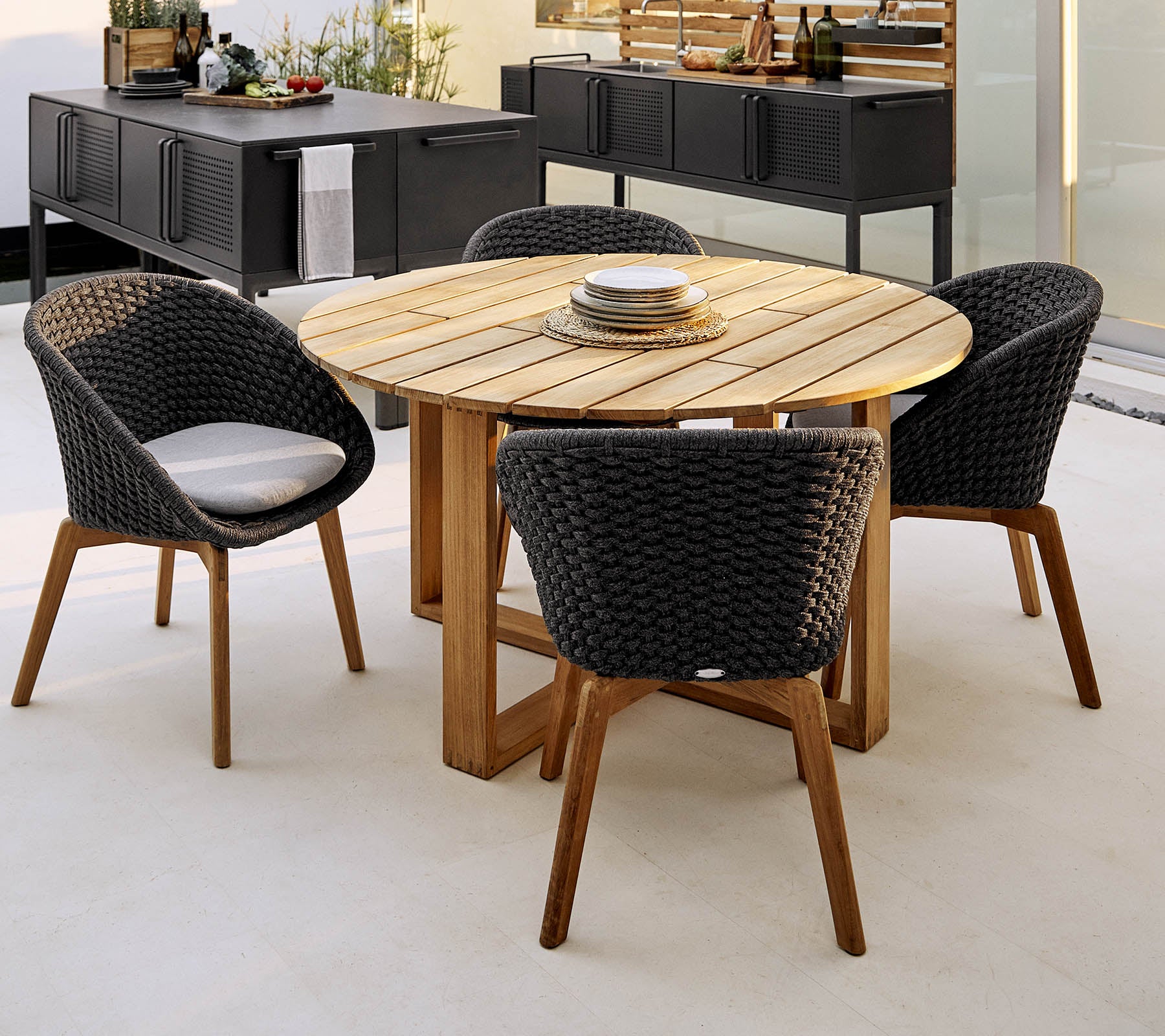 Table ronde en bois avec quatre chaises tressées élégantes, parfaite pour les dîners et les rassemblements sociaux. Agencement de sièges extérieur élégant et accueillant.